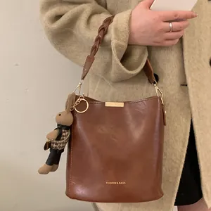 Vintage brown leather bucket bag with woven handle and plush rabbit charm on beige coat