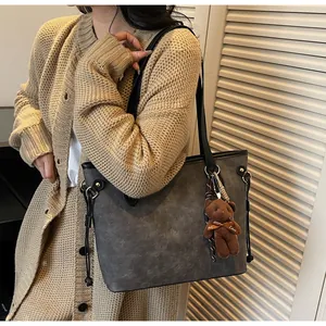 Detailed view of grey tote bag with embossed pattern and plush bear charm decoration