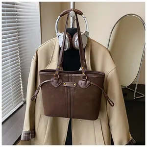 Détail d'un cabas en daim marron foncé avec cordons latéraux et plaque de logo en métal