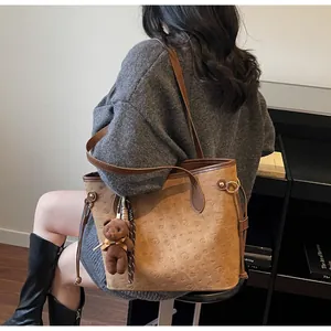 Brown embossed tote bag with teddy bear pendant shown on shoulder in daily life scene