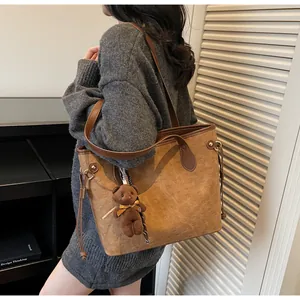 Detail of brown tote bag featuring dog embossed pattern and plush bear charm