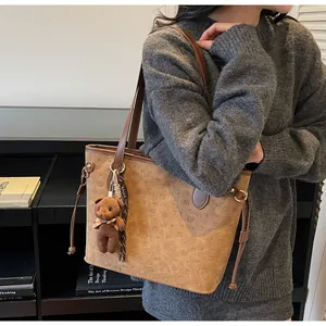 Detailed view of brown tote bag featuring cartoon dog embossing and plush bear charm
