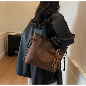 Detail of dark brown embossed tote bag featuring a cute plush bear charm and side drawstring