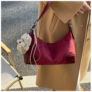 Detail of burgundy suede dumpling bag with plush bear charm and leather stitching