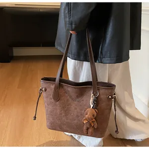 Detail of embossed cartoon patterns on brown tote bag with plush teddy bear charm