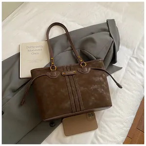 Détail d'un cabas en daim marron foncé avec plaque métallique et lanières latérales