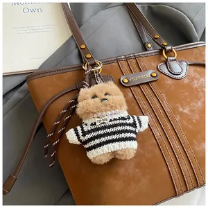 Gros plan d'un bijou de sac chiot en peluche avec pull rayé sur un sac en cuir