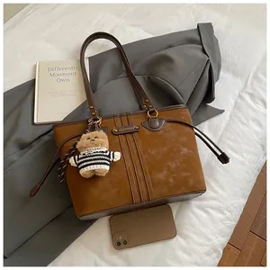 Vue à plat d'un grand sac cabas en daim marron avec pendentif ours et blazer gris