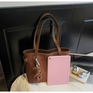 Detail of brown tote bag with cartoon bear embossing and plush charm next to a tablet