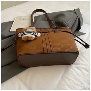 Détail du sac cabas en daim marron avec coutures, logo en métal et breloque ours
