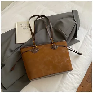 Détail d'un cabas en daim marron avec lanières en cuir et anneaux dorés sur un blazer gris