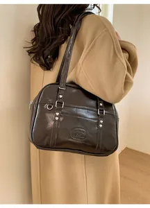 Détail du sac à bandoulière en cuir marron foncé avec rivets cœur et logo de marque
