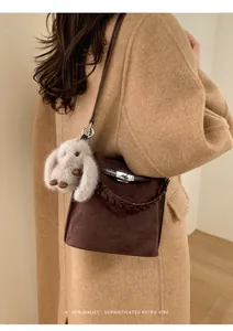 Detail of dark brown matte bucket bag with silver clasp and plush rabbit pendant charm