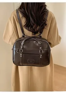 Sac à dos marron brillant avec rivets en forme de cœur porté sur un manteau beige