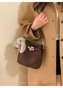 Detail of a dark brown suede bucket bag featuring a silver twist lock and woven leather handle