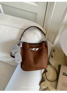 Detail of dark brown faux suede bucket bag with woven handle and elegant metal twist lock
