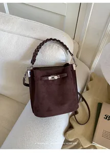 Detail of dark brown bucket bag with braided handle and metallic buckle on soft sofa