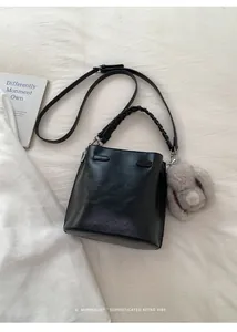 Detail of black bucket bag featuring woven handle and a grey plush bunny pendant