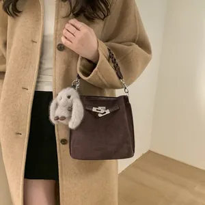 Brown suede bucket bag with woven handle and plush rabbit charm on a khaki coat