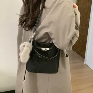 Black bucket bag with woven handle and plush rabbit charm shown on model