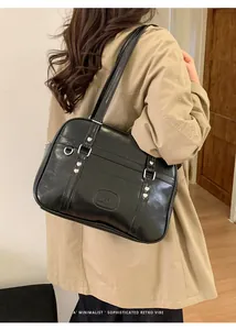 Détail du sac bandoulière noir brillant avec clous en cœur sur un modèle en trench