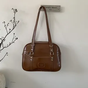 Détail du sac en cuir marron avec rivets coeurs argentés et logo embossé de marque élégant