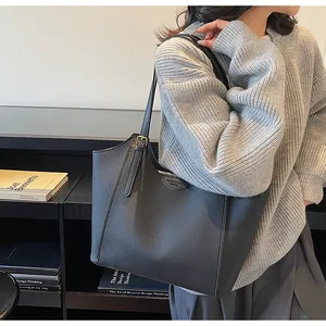 Detail of dark grey litchi grain leather tote bag with debossed label and gold hardware