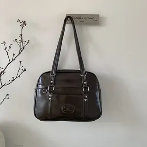 Détail du sac en cuir marron foncé avec rivets coeur argentés et design rétro rectangulaire