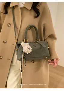Detail of retro sage green satchel with RSH logo and white plush puppy charm on coat