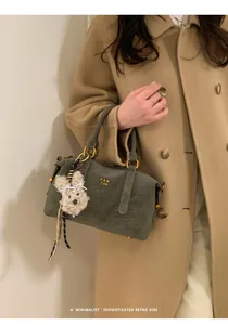 Close-up of olive green Boston bag with gold logo and plush poodle charm on wool coat