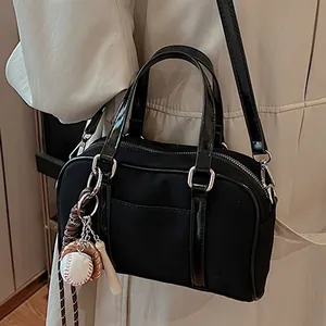 Borsa bowling nera in tessuto opaco con ciondoli da baseball su un trench beige