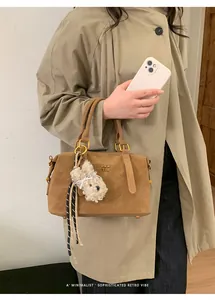 Detail of caramel suede handbag featuring a gold ring clasp and white plush charm
