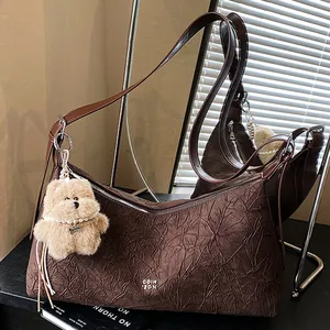 Deep brown pleated tote bag with plush bear charm and dual straps in a modern setting