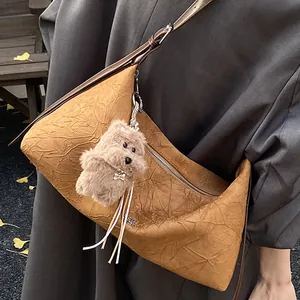 Brown pleated leather crescent shoulder bag with plush dog charm in an autumn park