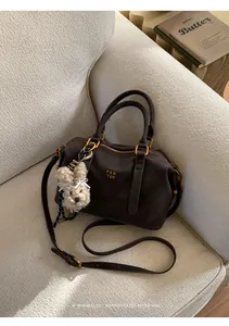Detail of dark brown leather Boston bag with plush rabbit charm on a cozy sofa