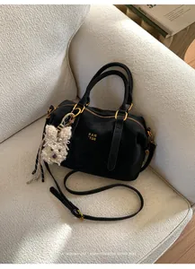 Detail of black Boston bag with gold hardware and white plush dog charm on sofa