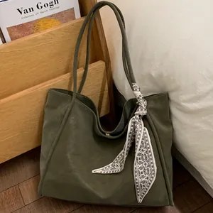 Large olive green faux leather tote bag with geometric silk scarf on wooden background