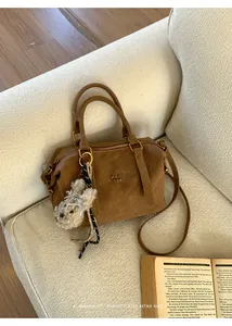 Close-up of brown Boston bag with PAN 'TOR logo and white bear charm on a cozy sofa
