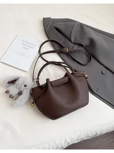 Detail of dark brown leather bucket bag with litchi texture and rabbit charm on white sheet