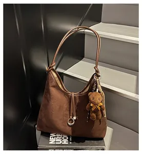 Detail of brown suede tote bag featuring a cute plush bear charm and metallic ring