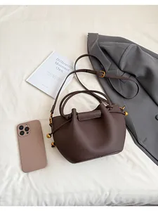 Close-up of brown pleated bucket bag with litchi texture and gold spherical drawstring detail