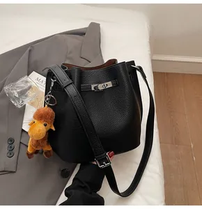 Detail of black lychee grain leather bucket bag with silver lock and camel plush charm