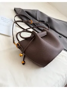 Detail of dark brown lychee leather bucket bag with gold hardware and drawstring