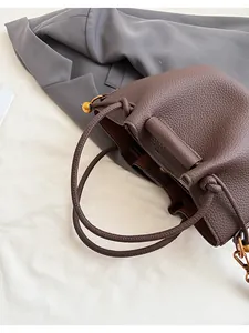 Close-up of deep brown lychee texture leather handbag with woven handle and gold hardware