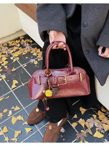 Detail of burgundy leather handbag with golden buckle and plush charms on ginkgo leaves