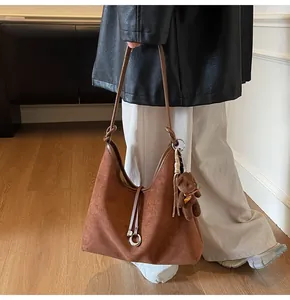Detail of brown suede tote bag featuring a long strap and a plush bear charm accessory