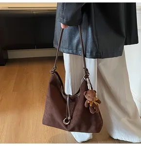 Close-up of brown suede tote bag with leather straps and a plush bear pendant
