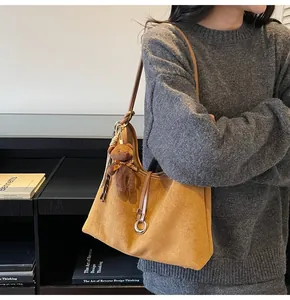 Detail of suede hobo bag with leather shoulder strap and plush bear keychain