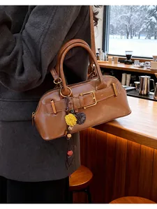 Close-up of brown leather shell bag with gold buckle and floral charm in cafe setting