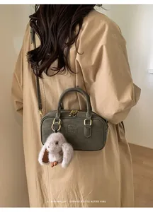 Detail of green bowling bag with gold zipper and plush rabbit charm on trench coat